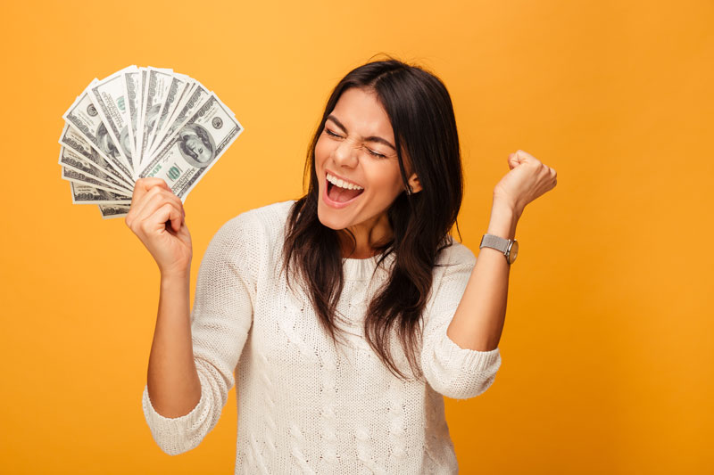 Woman celebrating while holding cash against a bright background, representing financial savings and tax benefits.